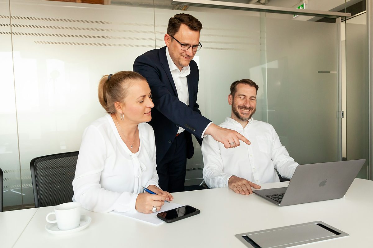 A trainer explaining something on a laptop to two employees at a meeting table